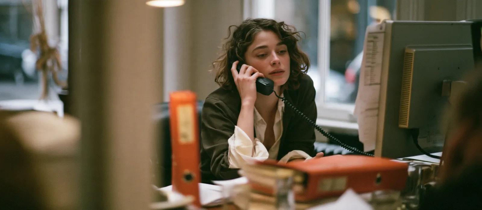 Insurance account handler at her office desk on a phone call, looking at a renewal list on her screen